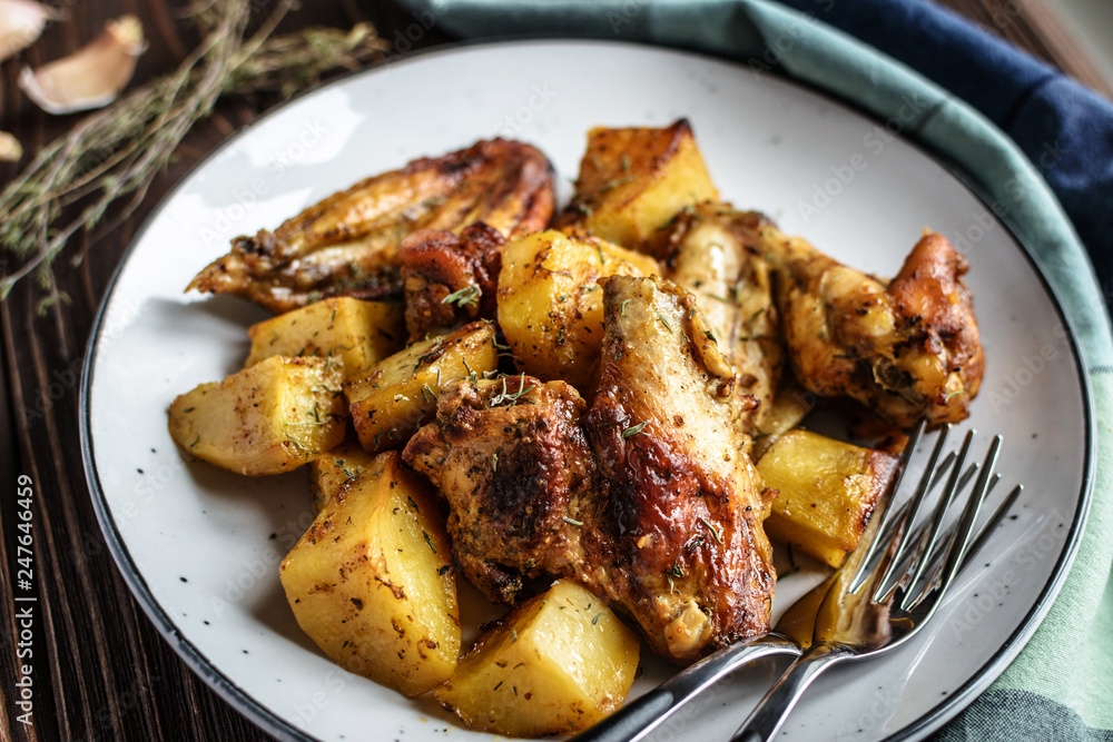 Baked chicken wings with potatoes and garlic on a rustic background Baked chicken wings with potatoes and garlic on a rustic background