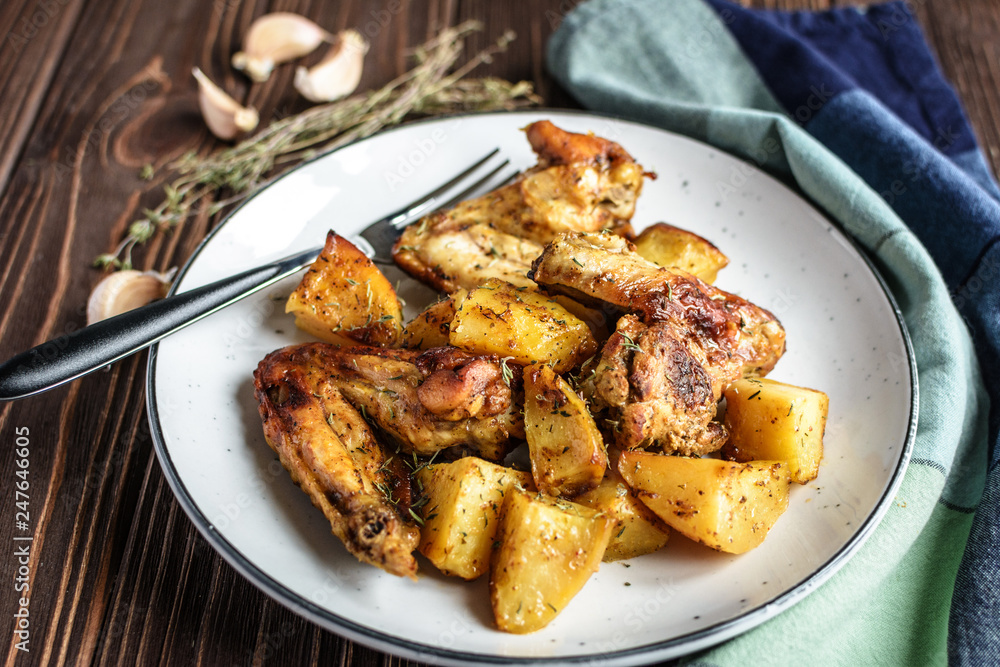 Baked chicken wings with potatoes and garlic on a rustic background Baked chicken wings with potatoes and garlic on a rustic background