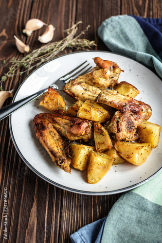 Baked chicken wings with potatoes and garlic on a rustic background