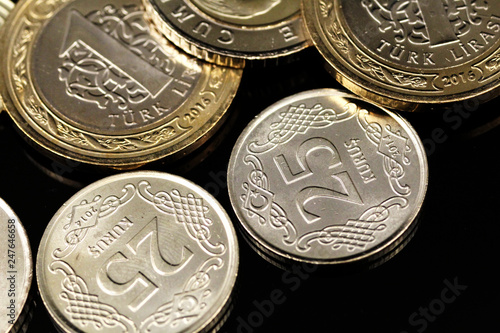 A macro image of an assortment of Turkish coins and a silver Chinese one ounce coin on a reflective black background