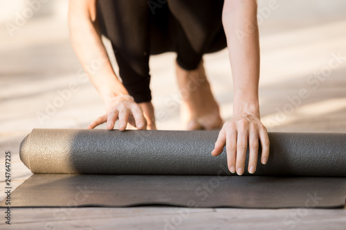 Close up of sportive female rolling yoga mat after training