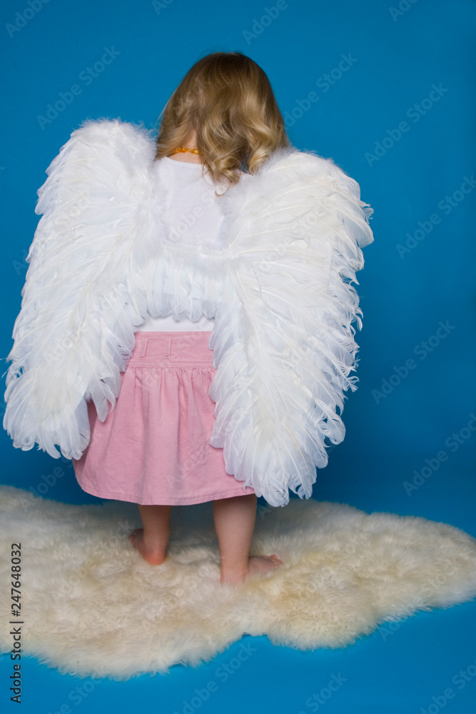 Kleines blondes Mädchen mit Engelsflügeln von hinten vor blauem Hintergrund Kleines blondes Mädchen mit Engelsflügeln von hinten vor blauem Hintergrund