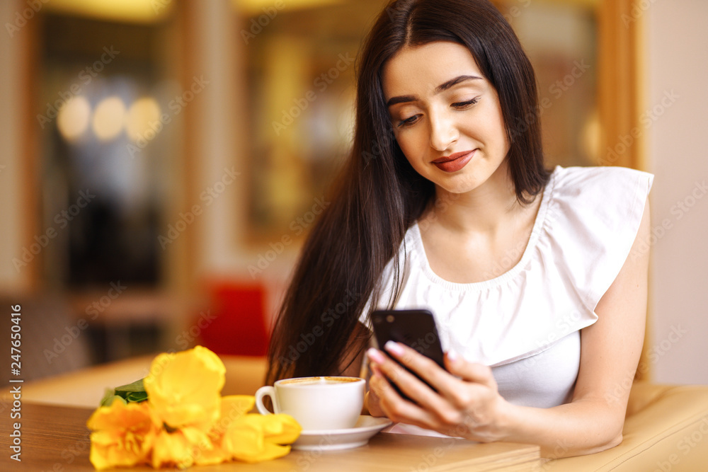 Beautiful Young Woman With Spring Tulips Flowers Bouquet At Cafe. Woman Drinking Coffee And Using Phone. Spring Style. Brunette Woman In Nice Spring.Beautiful Spring Mood. Fashion Spring/Summer. Beautiful Young Woman With Spring Tulips Flowers Bouquet At Cafe. Woman Drinking Coffee And Using Phone. Spring Style. Brunette Woman In Nice Spring.Beautiful Spring Mood. Fashion Spring/Summer.