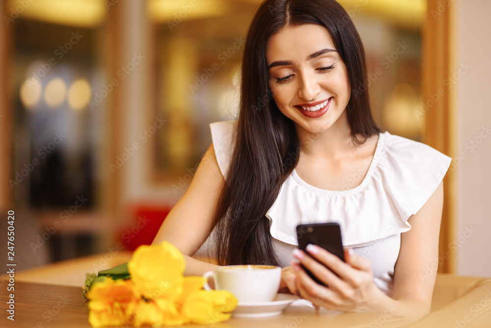 Beautiful Young Woman With Spring Tulips Flowers Bouquet At Cafe. Woman Drinking Coffee And Using Phone. Spring Style. Brunette Woman In Nice Spring.Beautiful Spring Mood. Fashion Spring/Summer. Beautiful Young Woman With Spring Tulips Flowers Bouquet At Cafe. Woman Drinking Coffee And Using Phone. Spring Style. Brunette Woman In Nice Spring.Beautiful Spring Mood. Fashion Spring/Summer.