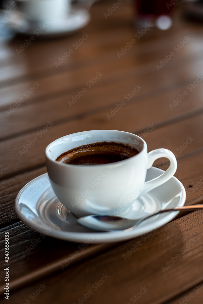 A small white porcelain espresso cup on a saucer with a teaspoon and two pieces of sugar