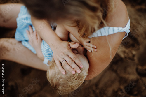 A young mother breasfeeding toddler daughter on beach on summer holiday. photo