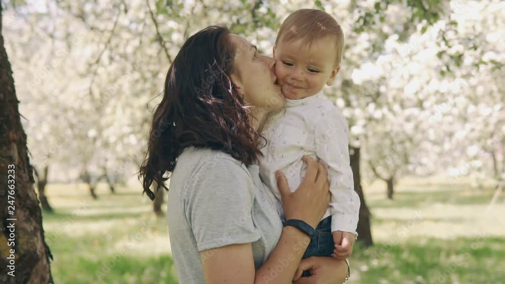 Brunette young mother and baby laughing together while playing outdoors. Mother holding and kissing her little son. Mom showing love and affection to son. Motherhood concept in slow motion Brunette young mother and baby laughing together while playing outdoors. Mother holding and kissing her little son. Mom showing love and affection to son. Motherhood concept in slow motion
