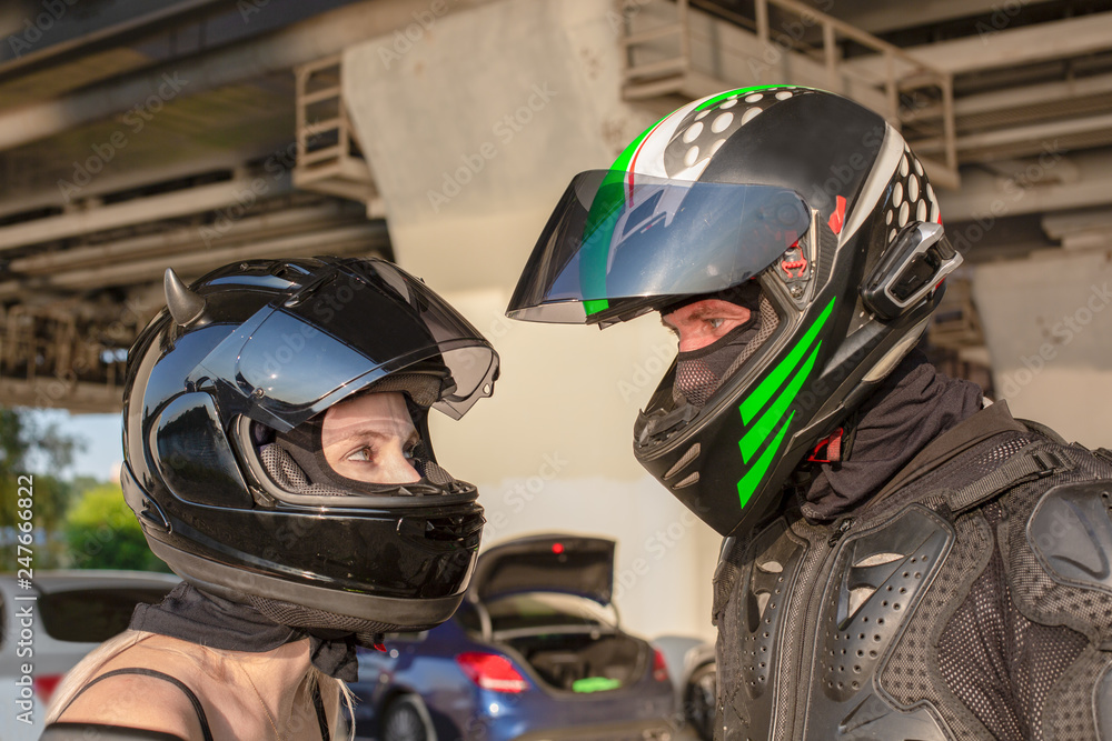 Portrait of bikers man and woman in helmets look at each other. Motorcycle love concept. Extreme riders Portrait of bikers man and woman in helmets look at each other. Motorcycle love concept. Extreme riders