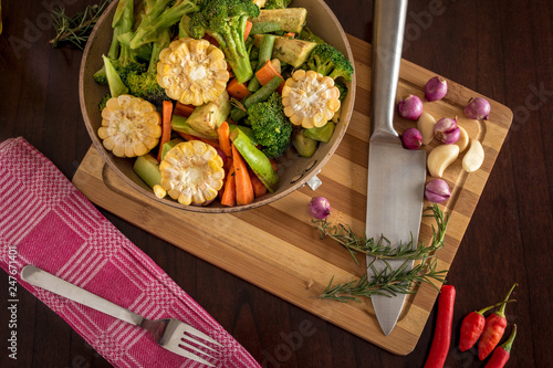 Roast vegetables, herbs and spices on chopping board with knife, food and cooking stock lay flat image.