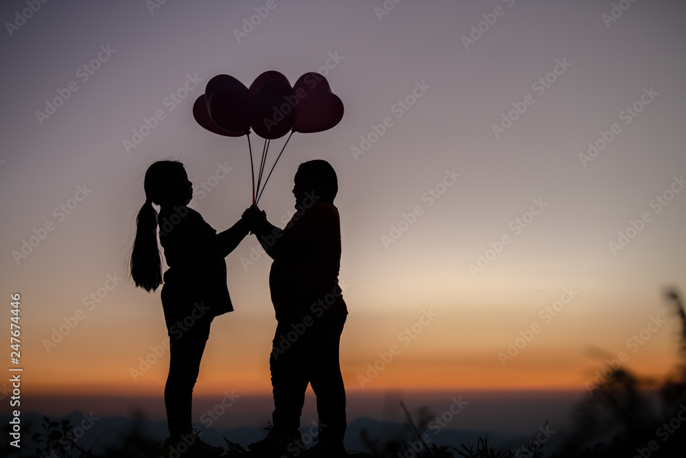 The silhouette of a lover rubs him at sunset, a love story of a man and a woman on a mountain, a beautiful couple in the sun, a balloon.