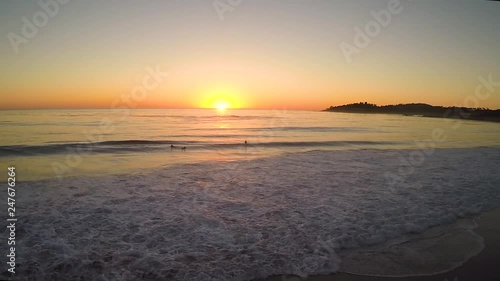 The camera pulls back to reveal a silhouetted surfer standing on the beach watching the dramatic sunset over Carmel beach in California.