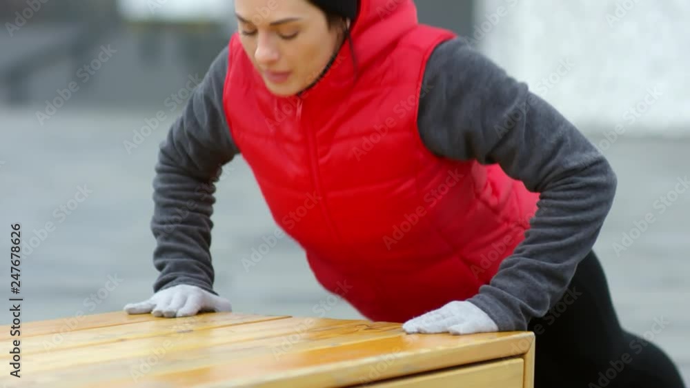 Medium shot of motivated fit young woman in sports clothes practicing push ups exercise on bench outdoors Medium shot of motivated fit young woman in sports clothes practicing push ups exercise on bench outdoors