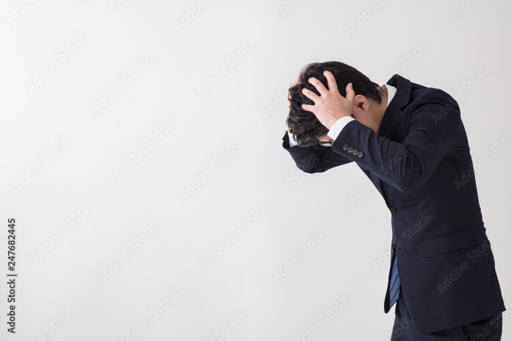 白背景でスーツの男性が頭を抱えてショックを受けている場面 白背景でスーツの男性が頭を抱えてショックを受けている場面
