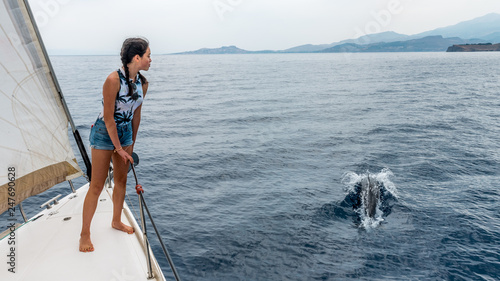 young teen standing on the deck of a sailboat with dolphin