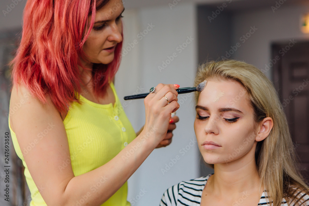 Make-up artist doing make up to the model in studio.