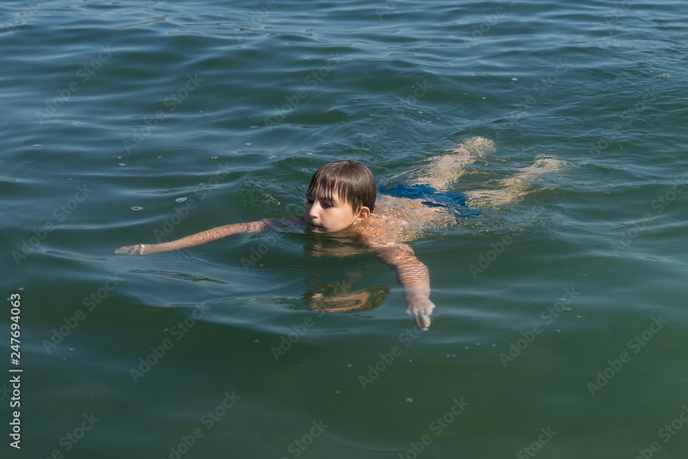 A boy of 11 years old is swimming in the blue water of a natural reservoir.