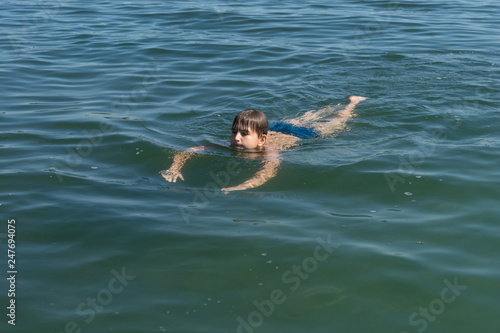 A boy of 11 years old is swimming in blue water.