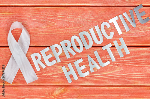white awareness ribbon and inscription of iron letters: reproductive health, lying on wooden textured background color of season 2019