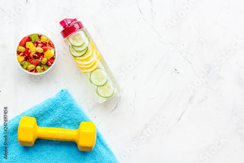 Healthy lifestyle, healthy habits. Detox water, fruit salad, sport equipment dumbbells on white stone background top view copy space