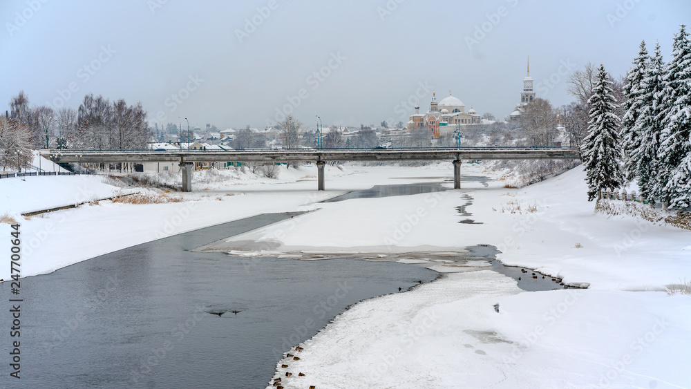 winter view of a frozen river covered with snow, a bridge over it and an old orthodoxal monastery on the right bank