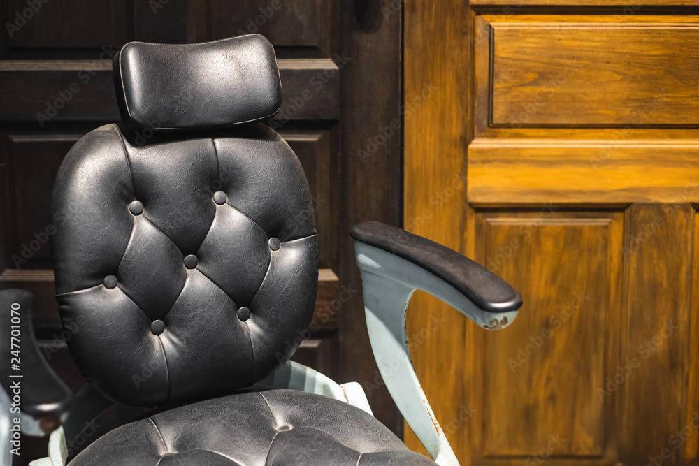 A leather chair with armrest in front of wood panel A leather chair with armrest in front of wood panel