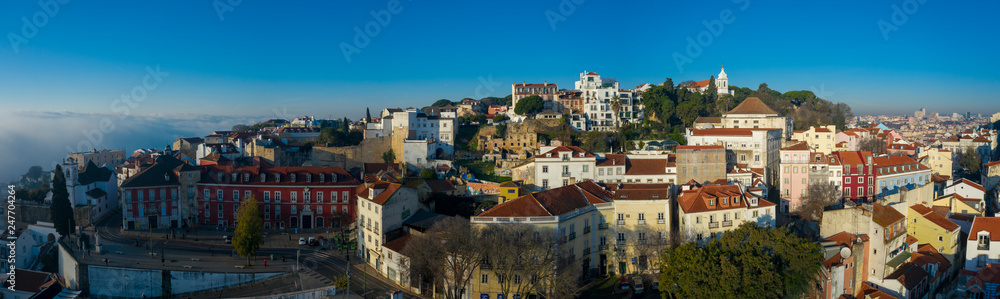 Beautiful panoramic Lisbon landmark with tiny houses with moorish architectural elements on the hill; drone view of picturesque labyrinth of narrow streets and small squares in early morning, Portugal