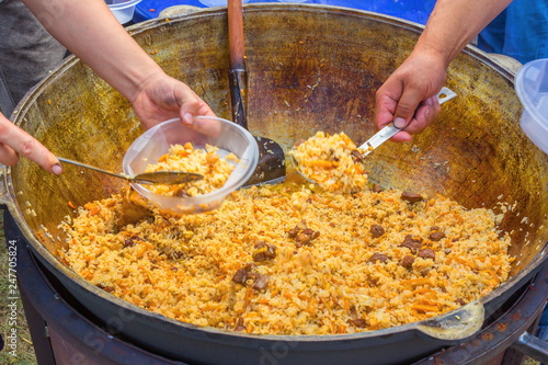 Russia, Samara, July, 2018: Uzbek cook lays out cooked pilaf in plates during the holiday. Ethno-historical festival with the reconstruction of the battle of 1391 (Timur and Tokhtamysh) photo