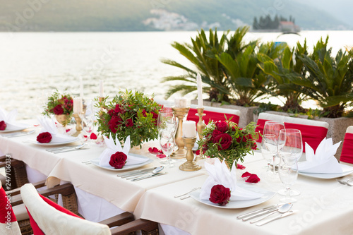 table for a wedding dinner decorated with red flowers and greenery