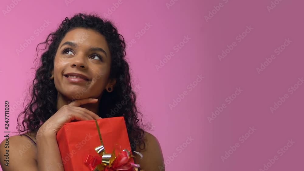 Afro-American woman holding giftbox and looking up, dreaming about romantic date Afro-American woman holding giftbox and looking up, dreaming about romantic date