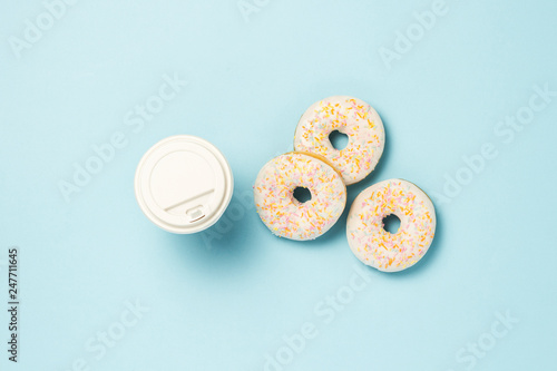 Fresh tasty sweet donuts and a paper cup of coffee or tea on a blue background. Fast food concept, bakery, breakfast,. Minimalism. Flat lay, top view.