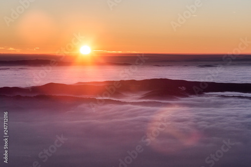 Beautiful sunset over a valley filled by fog with mountains and hills © Massimo
