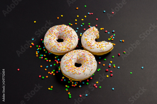 Delicious, sweet, fresh donuts and multicolored decorative candies on a black background. Breakfast concept, fast food, coffee shop, bakery.