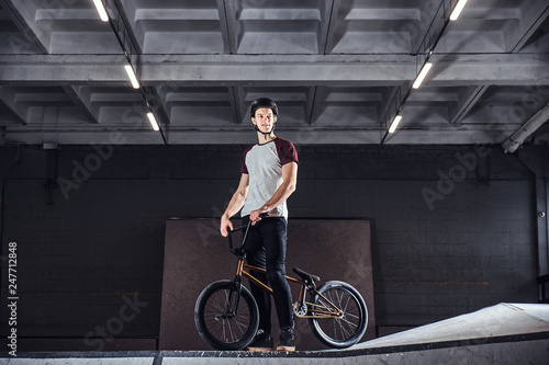 Professional BMX rider in protective helmet getting ready to jump in a skatepark indoors