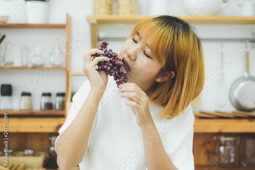 Asian beautiful woman eat grape in the kitchen at her home. Happy pretty Asian female eat freshness fruit for healthy body. lifestyle asia woman at home concept.