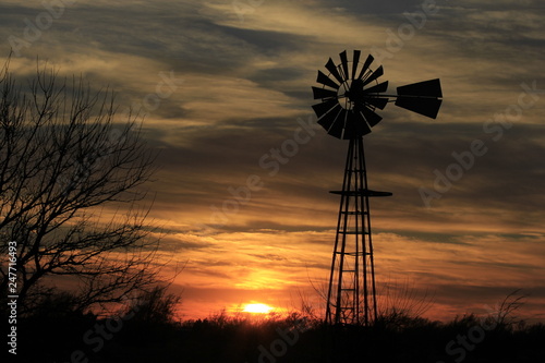 windmill at sunset with clouds and trees.