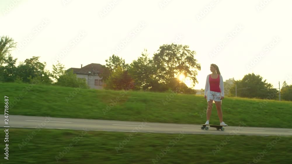 SUN FLARE: Carefree female skateboarder riding her e-longboard on a beautiful sunny morning. Cool girl speeding down empty concrete track and past a lush green park on a high tech electric skateboard. SUN FLARE: Carefree female skateboarder riding her e-longboard on a beautiful sunny morning. Cool girl speeding down empty concrete track and past a lush green park on a high tech electric skateboard.