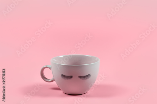 Cute pink coffee or tea mug with false lashes on a pink background. Morning energy. Female cute background.