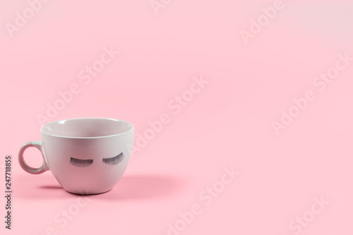 Cute pink coffee or tea mug with false lashes on a pink background with copy space. Morning energy. Female cute background.