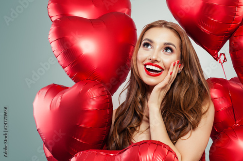 Excited young woman holding balloons red heart. Surprised girl with red lips makeup, long curly hair and cute smile