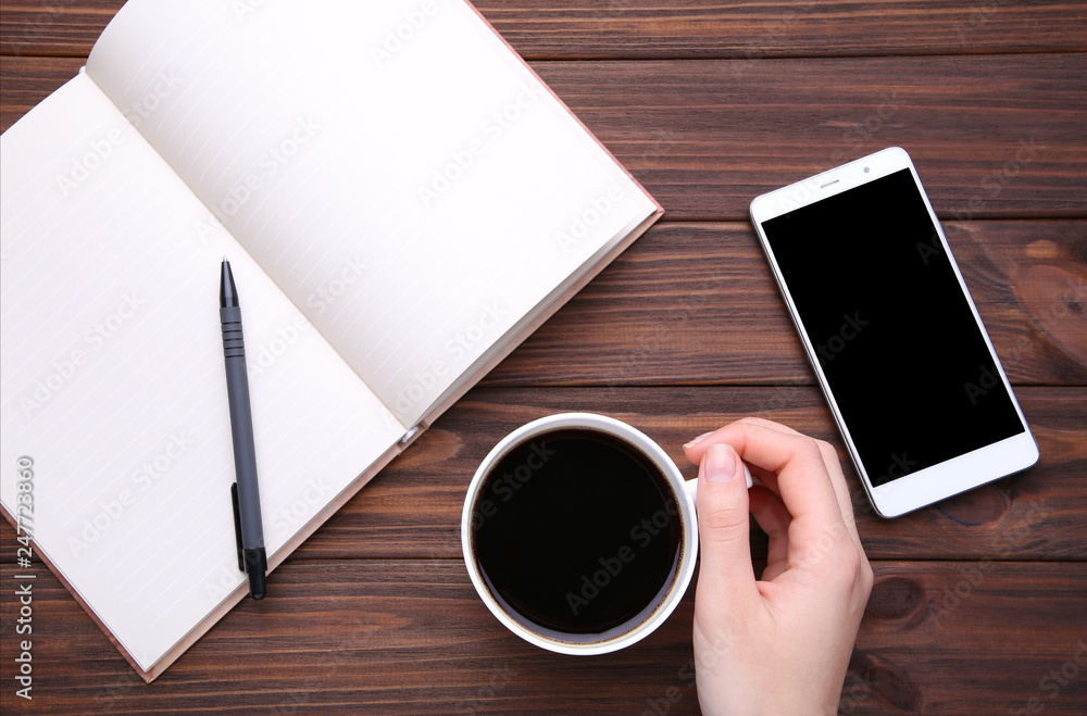 Female hands holding cup of coffee and smartphone on brown wooden background. Female hands holding cup of coffee and smartphone on brown wooden background.