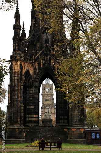 Scott Monument on Edinburgh's Princess Street, a Victorian Gothic monument to Scottish author Sir Walter Scott with clocktower at the center and bench with two people at in the foreground.