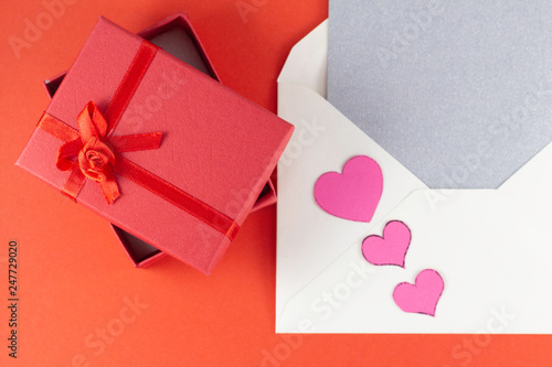 Silver open envelope with white blank letter and three small pink hearts Big red open gift box Red background Invitation Minimalist concept Copy Space and template © Igor Zaharov