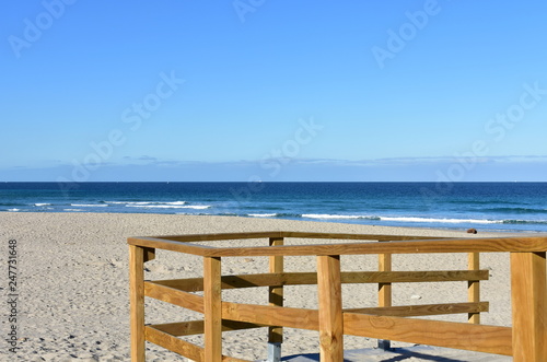 Beach with wooden handrail and morning light. Golden sand and blue sea with waves and white foam. Sunny day  Galicia  Spain.