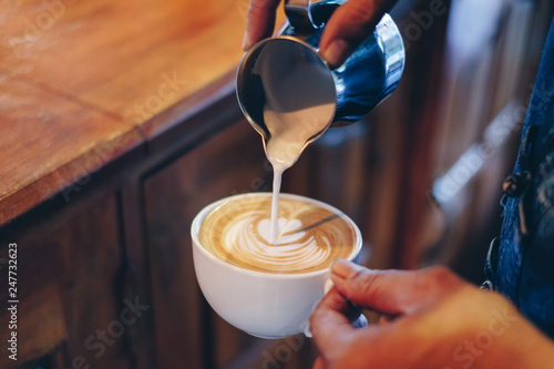 Quadro em tela Hand barista pouring milk on coffee latte flower shape in cup