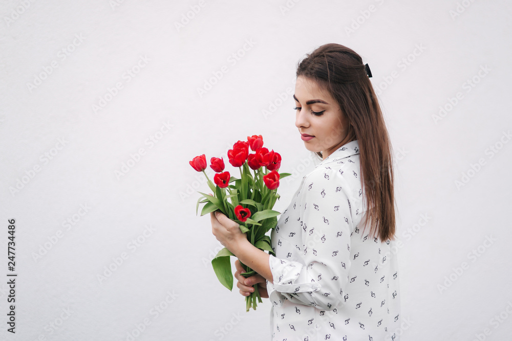Attractive young lady in white shirt hold a bouquet of red flowers. White background Attractive young lady in white shirt hold a bouquet of red flowers. White background