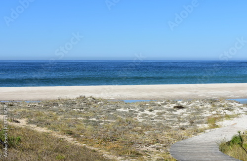 Beach with wooden boardwalk and sand dunes with grass. Blue sea and clear sky  sunny day. Galicia  Spain.