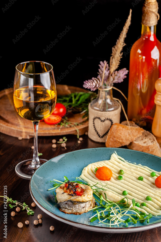 The concept of Italian cuisine. Baked Seabass Fish with Vegetables and Mashed Potatoes. A glass of white wine on the table. Servovika dishes in the restaurant. copy space
