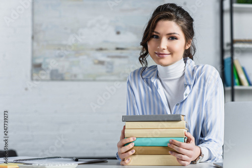 cheerful woman sitting near books in modern office