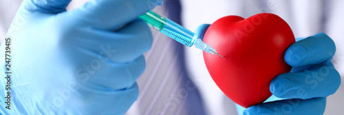 Physician arms wearing protective blue gloves stick needle into heart