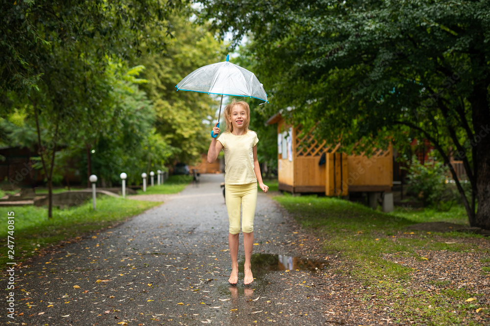 Blonde girl with umbrella jumping on the puddles